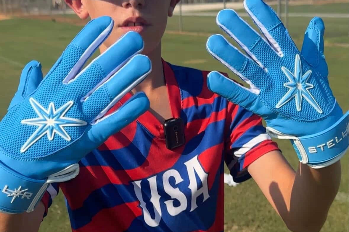Person wearing blue gloves with a star design, holding them up, on a grassy field.