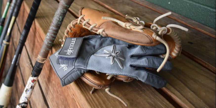 A pair of stylish batting gloves resting on a wooden surface next to baseball bats and a glove.