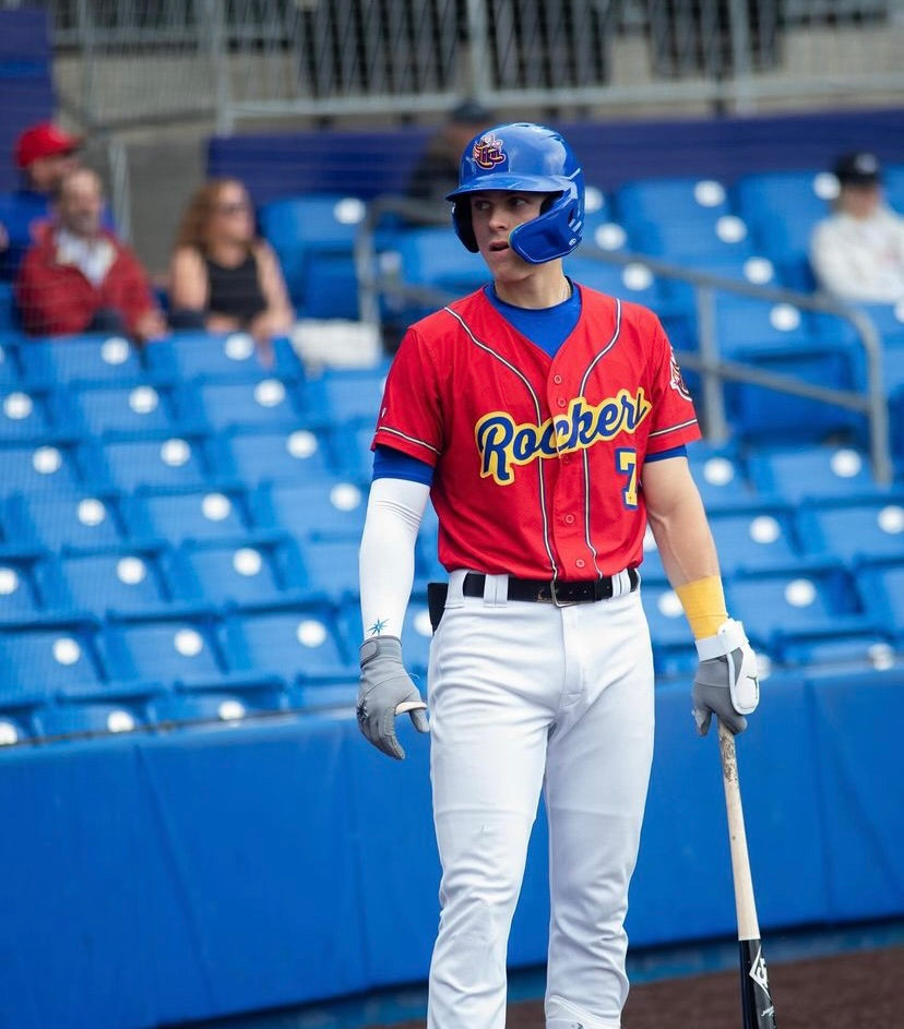 Baseball player in a red Rockers jersey with sleeves, preparing at bat during a game.