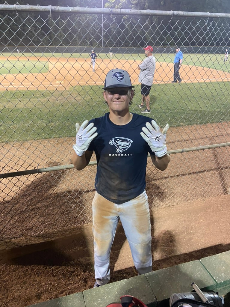 Person on a baseball field wearing a navy blue shirt with a logo and white gloves.