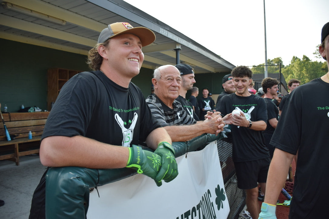 Man in black shirt and green gloves holding a banner with people in the background